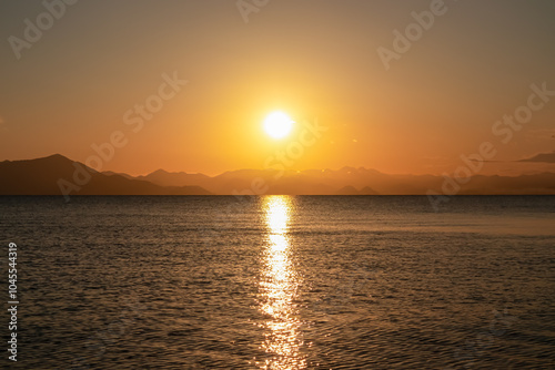 Breathtaking sunset over calm Skadar lake, Albania. Sun is setting behind Dinaric Alps mountains in Montenegro. Water reflects vibrant colors of sky creating shimmering path across the surface
