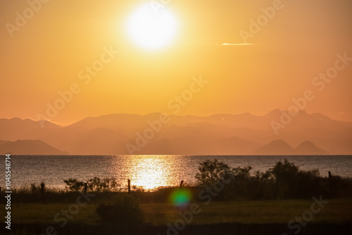 Breathtaking sunset over calm Skadar lake, Albania. Sun is setting behind Dinaric Alps mountains in Montenegro. Water reflects vibrant colors of sky creating shimmering path across the surface photo