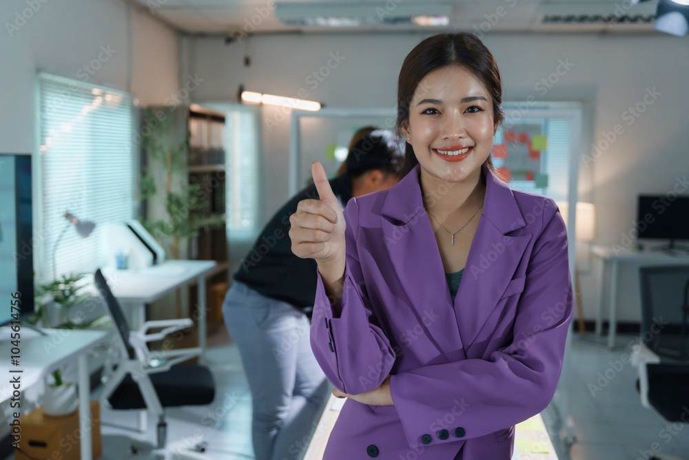 Asian businesswoman is smiling while giving a thumbs up gesture of approval in a modern office Asian businesswoman is smiling while giving a thumbs up gesture of approval in a modern office