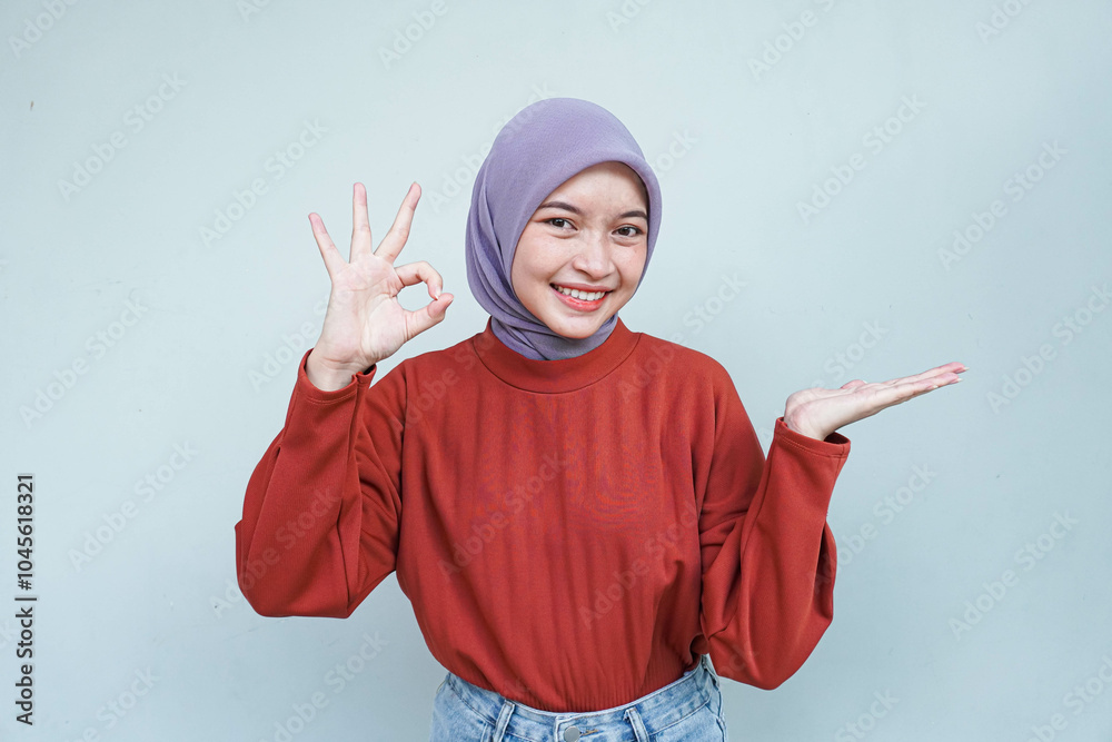 Beautiful smiling Asian woman in red sweater showing okay and pointing or showing gesture demonstrates symbol of approval isolated over gray background. Beautiful smiling Asian woman in red sweater showing okay and pointing or showing gesture demonstrates symbol of approval isolated over gray background.