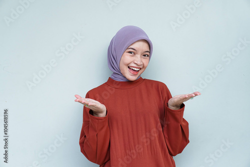 Happy young Asian Muslim woman wearing hijab with welcome gesture. Isolated white background.