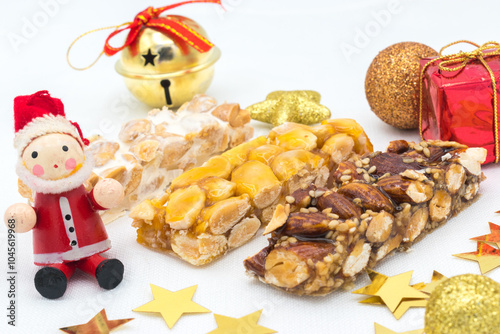 Different types of turrón (nougat), a traditional Christmas sweet in Spain, with some Christmas decoration ( a wooden Santa Claus, a gift box, a jingle bell and some stars), on a white background. photo