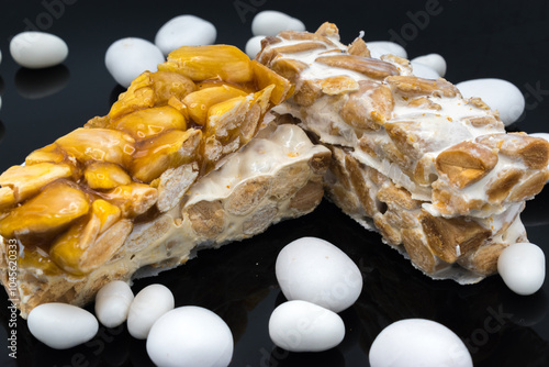 Different types of turrón (nougat), a traditional Christmas sweet in Spain, isolated on a black surface, with some sugared almonds. photo