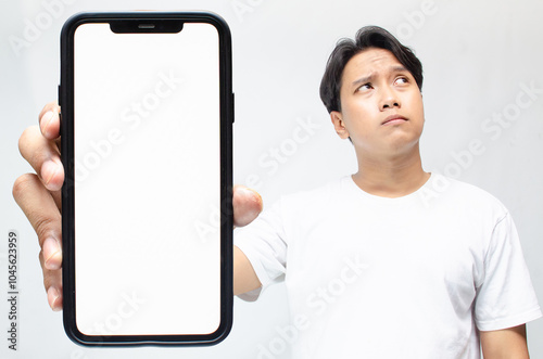 an overthinker young asian man thinking deeply while showing his big screen phone after receiving bad news. mock up of thoughtful asian man showing his blank screen phone