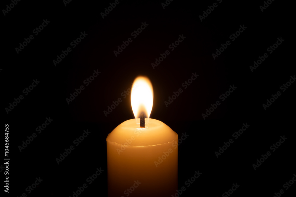 A single burning candle flame or light glowing on a big white candle isolated on red or dark background on table in church for Christmas, funeral or memorial service A single burning candle flame or light glowing on a big white candle isolated on red or dark background on table in church for Christmas, funeral or memorial service