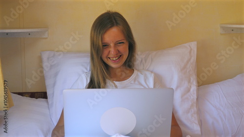 Young woman using laptop on bed, enjoying online communication. Relaxation and Technology