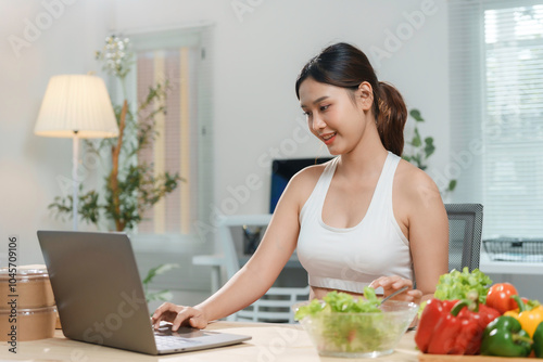 Young asian woman enjoying a healthy salad while working on her laptop, embracing a balanced lifestyle photo