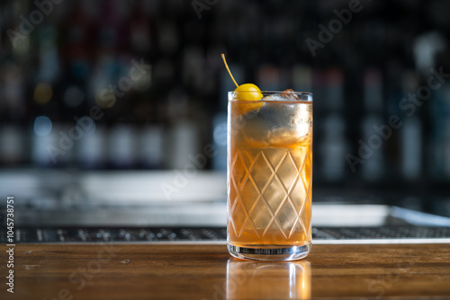 Highball glass with alcoholic cocktail decorated with a yellow cocktail apple served on counter of bar on blurred background with bokeh