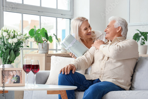 Mature woman greeting her husband with gift on their wedding anniversary at home