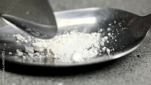 White pill being crushed under a spoon on black background, health care medicine concept, macro, close up