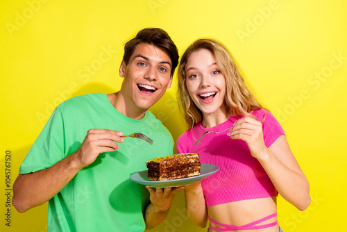 Portrait of two nice young partners eat cake wear t-shirt isolated on vibrant yellow color background photo