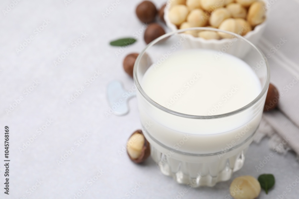 Glass of macadamia milk and nuts on white table, closeup. Space for text Glass of macadamia milk and nuts on white table, closeup. Space for text