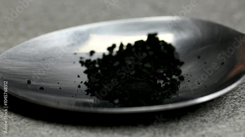 Black pill being crushed under a spoon on black background, health care medicine concept, macro, close up