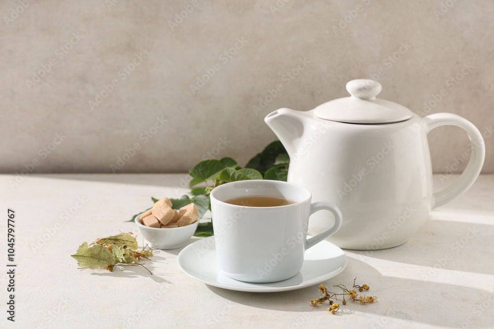 Cup of tasty linden tea with teapot and leaves on white background