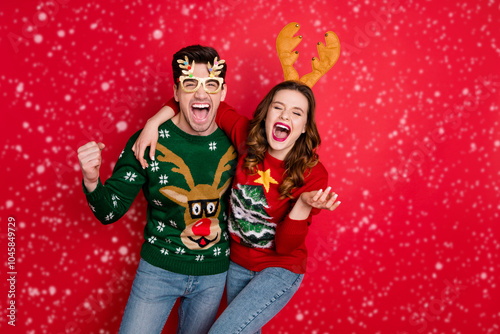 Photo of excited pair lady and guy chilling at newyear theme costume party wear funky knitted pullovers with ornaments isolated red color background photo