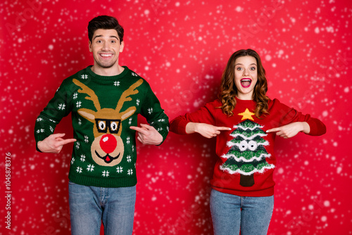 Look Midnight presents Portrait of two brunet hair lovers people scream wow omg point indexf inger his her reindeer christmas tree pattern pullovers wear jeans isolated over red color background photo