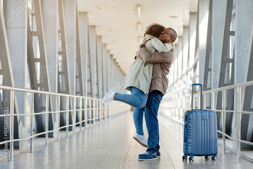 Loving Happy Young african couple embracing joyfully in the airport terminal, romantic man lifting woman off the ground, joyful spouses reunited after long time apart, happy to see each other, copy