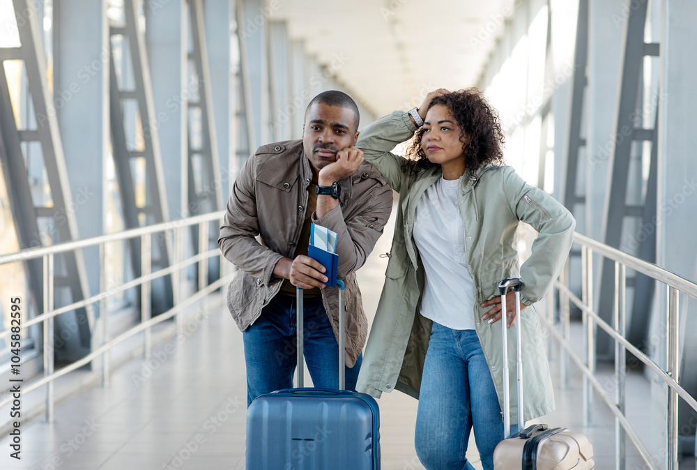 Upset African American Tourists Couple missed the flight or train, both standing next to a bright suitcase at a modern transit station. High quality photo