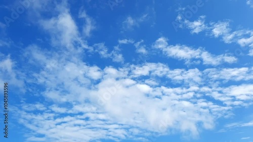 White clouds are rapidly floating across the blue sky. Against the background of a blue sky, clouds are moved by the wind