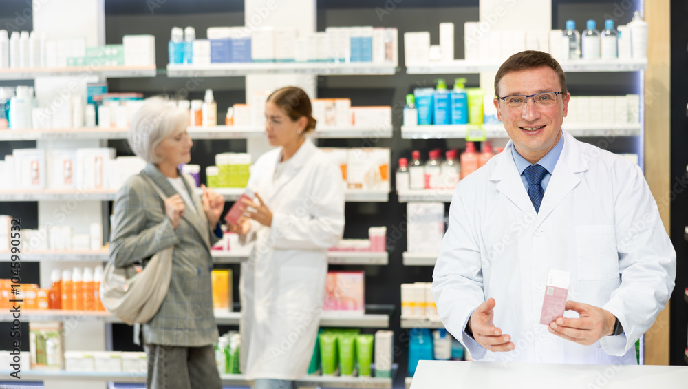 Fototapeta premium Portrait of man druggist in lab coat standing in drugstore with drug package