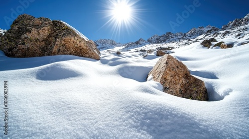 Sunlight illuminates a snowy mountain terrain with rugged rocks scattered across the landscape, conveying a raw yet stunning display of winter's grace. photo