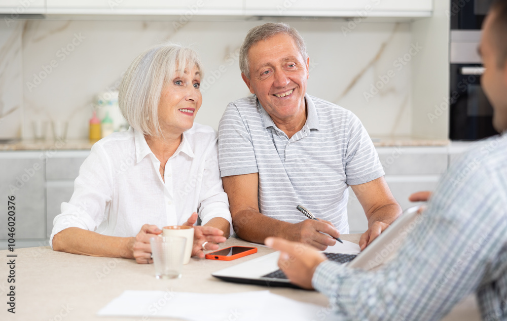 Obraz premium Couple of elderly man and woman discussing deal with male salesman in kitchen home