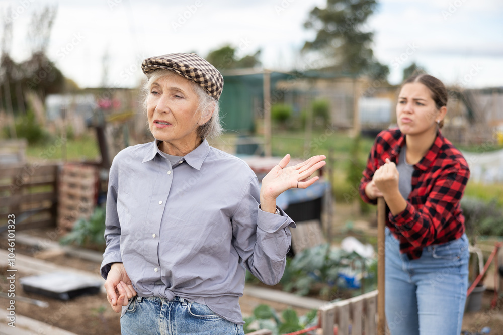 Φωτογραφία Two disappointed young and old female neighbors quarreling while digging garden