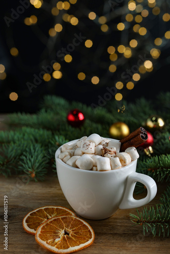 Tasty hot cocoa drink with marshmallows, cinnamon stick in cup and dry orange slices on wooden table, closeup