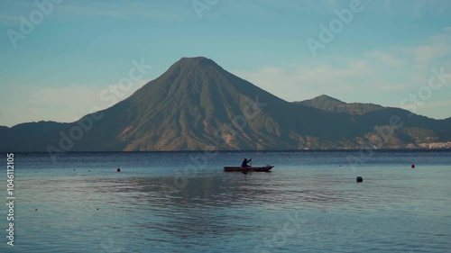 Man in his boat, preparing to fish in the calm dawn of Lake Atitlan. The soft light of the newly emerging sun illuminates the water as the volcanoes rise majestically on the horizon.
