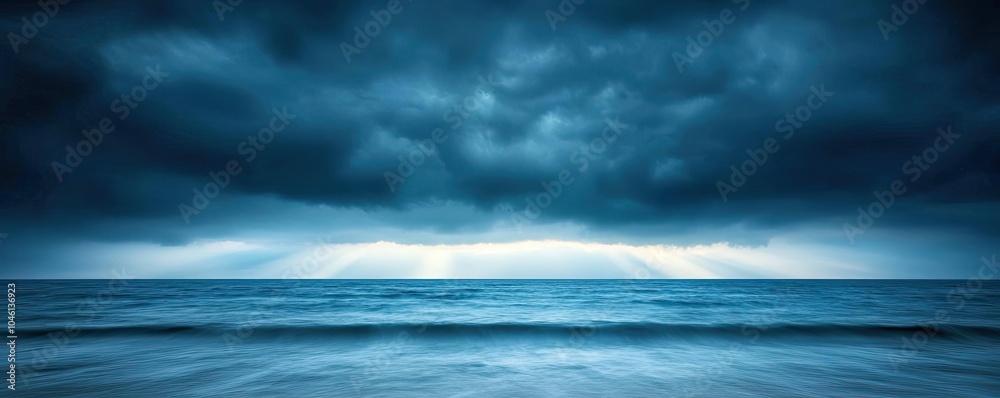 Obraz premium Dark stormy clouds above a calm ocean with gentle waves and distant light.