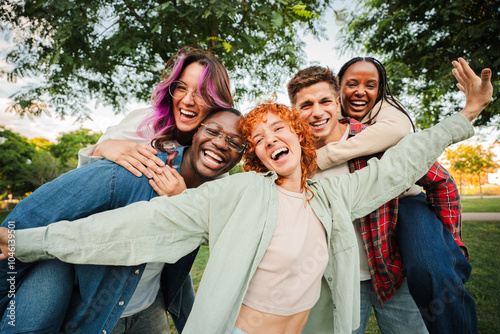 Group of joyful young friends having fun outdoors, embracing and laughing together in a park. Energetic, carefree and multiracial people enjoying a lively and playful moment of friendship