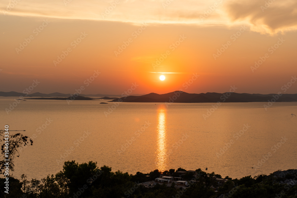 Fototapeta premium Beautiful sunset over tranquil sea with warm golden tones reflecting off the water and distant islands on the horizon. Peaceful landscapes. High quality photo