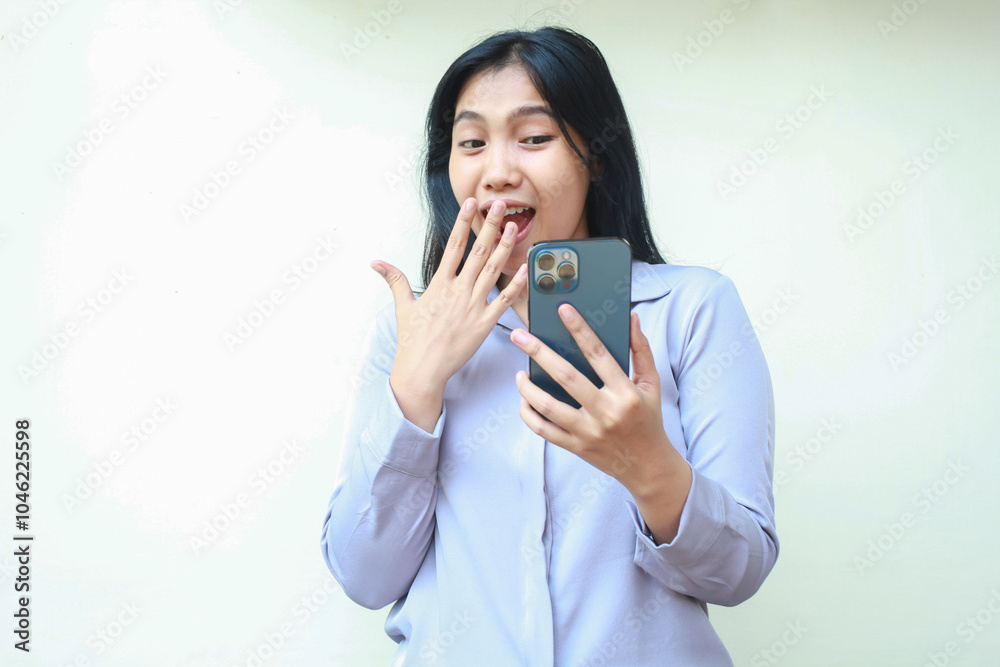 shocked asian young business woman stunned and covering her mouth while looking mobile phone wearing formal shirt standing over isolated white background shocked asian young business woman stunned and covering her mouth while looking mobile phone wearing formal shirt standing over isolated white background