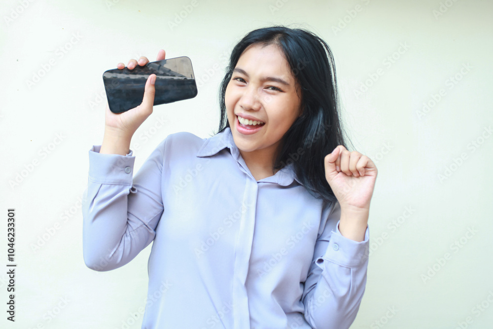 excited asian young business woman holding mobile phone and raising fist pump say yes gesture winning achievement, celebrate victory with dancing, wearing formal shirt standing over white background excited asian young business woman holding mobile phone and raising fist pump say yes gesture winning achievement, celebrate victory with dancing, wearing formal shirt standing over white background
