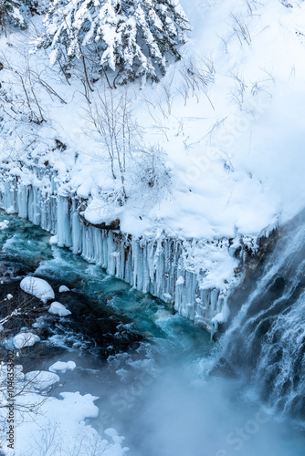 Aerial view of a frozen waterfall surrounded by snow-laden trees, showcasing the raw power of nature in winter.