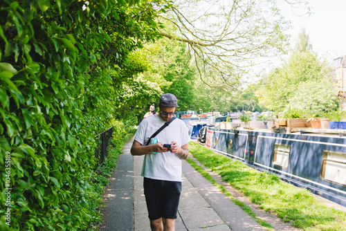 Fotografie Man Texting on Phone While Walking by Canal Boats