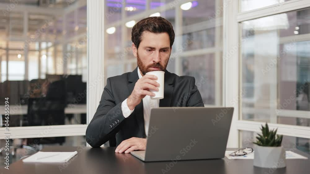 Businessman working on a laptop in an office. Manager, banking worker takes a sip of coffee while working. The office is modern and stylish. Businessman working on a laptop in an office. Manager, banking worker takes a sip of coffee while working. The office is modern and stylish.