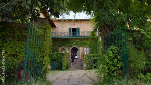 Static shot of a man in black walking down the stairs of a Tuscany villa, under summer sunlight, evoking mystery and elegance. photo