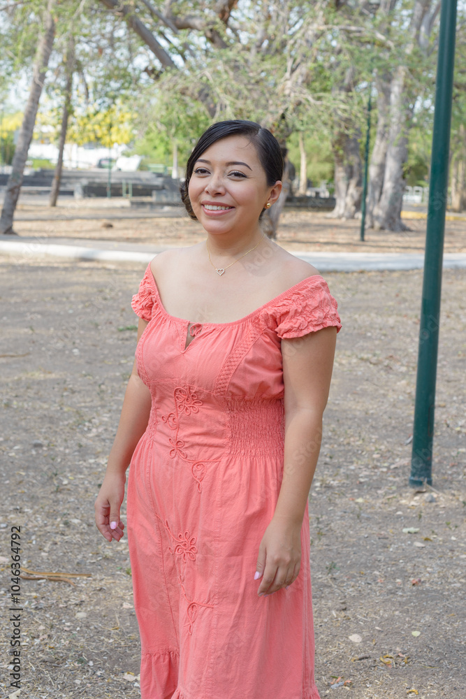 Fototapeta premium A dark-haired young woman smiling while wearing a coral dress with delicate embroidery.