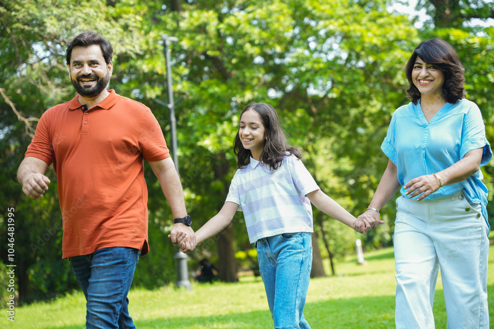 Happy young indian family of three walkin together at summer park have fun together. Asian Parents with daughter, Mom dad bonding with child. Parenthood. Togetherness. Love and Care. Happy young indian family of three walkin together at summer park have fun together. Asian Parents with daughter, Mom dad bonding with child. Parenthood. Togetherness. Love and Care.