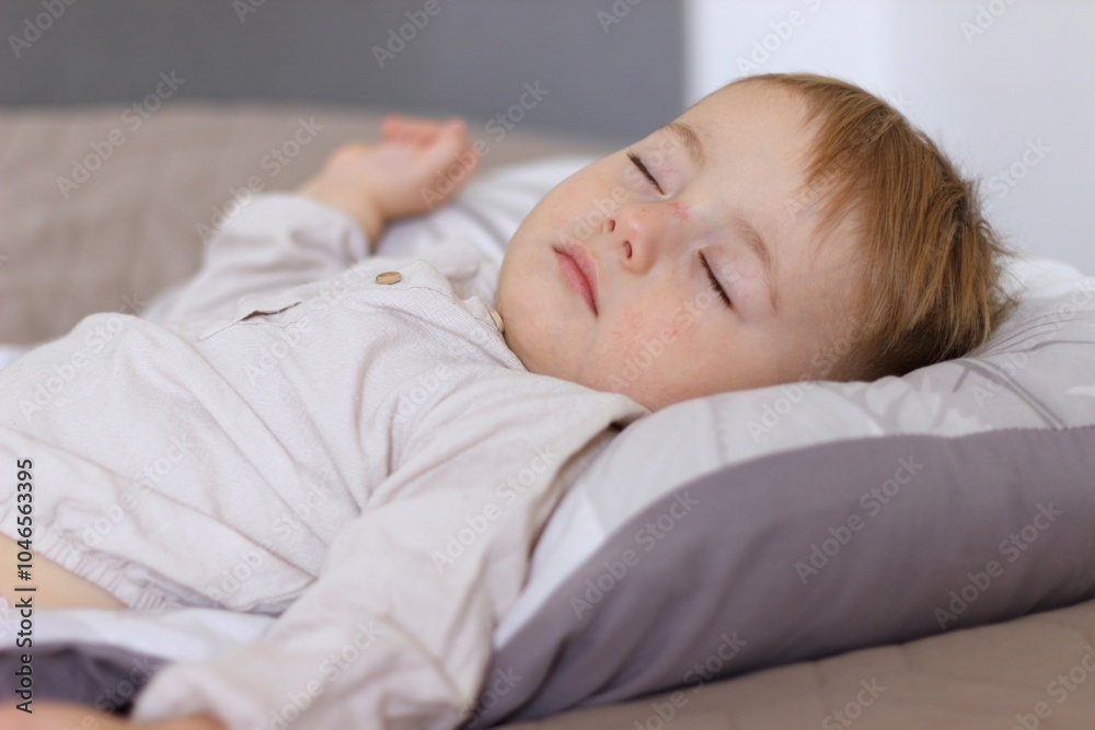 During the day, the child sleeps. The baby is daydreaming, he is lying on a light bed in a beige shirt During the day, the child sleeps. The baby is daydreaming, he is lying on a light bed in a beige shirt