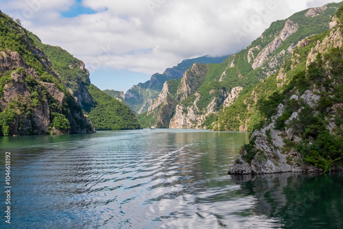 Scenic ferry boat tour on Lake Koman reservoir on Drin river surrounded by forested steep hills, cliffs and majestic rugged mountain ranges of Albanian Alps. Panoramic view along Albanian Fjords. Awe photo