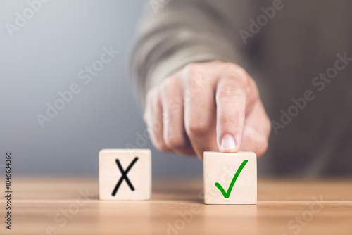 A man choosing between a checkmark and an 'X' symbol on wooden blocks. Image represents the concept of making the right choice, highlighting the importance of distinguishing between right and wrong photo