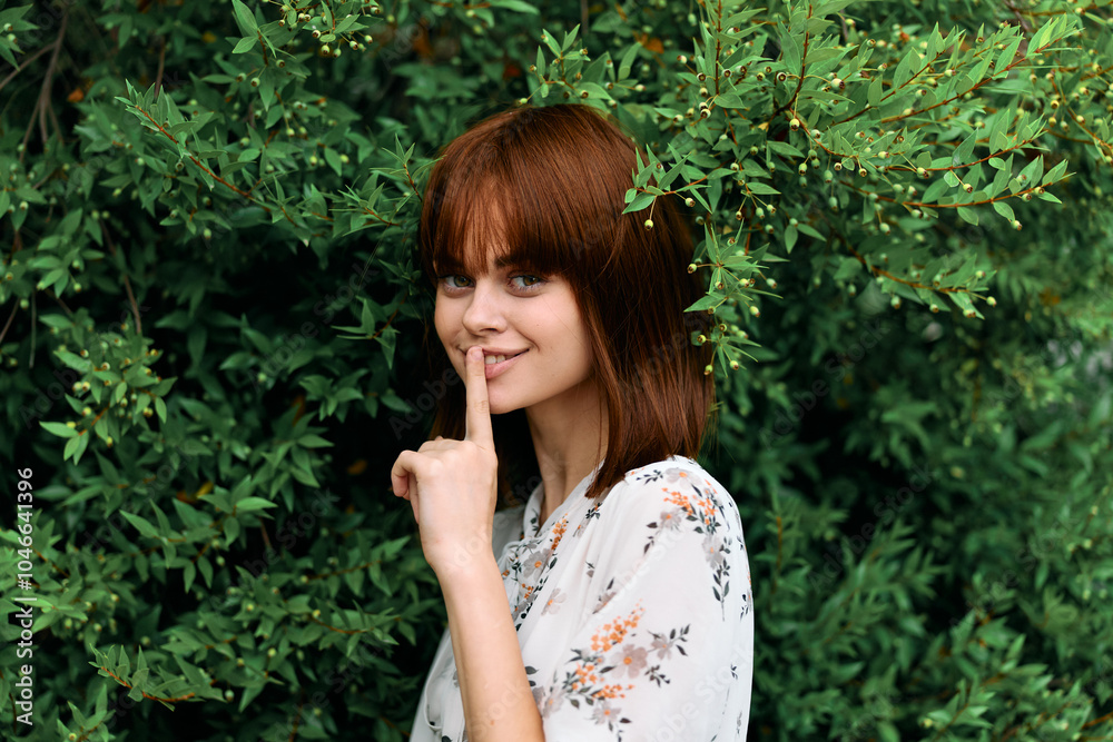 Silent gesture woman with finger on lips in front of lush green bush of leaves Silent gesture woman with finger on lips in front of lush green bush of leaves