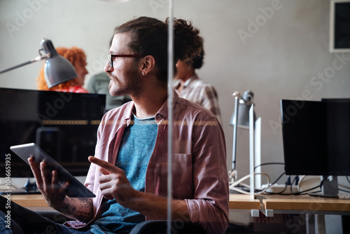 Happy young hipster businessman programmer holding a digital tablet and working in startup office