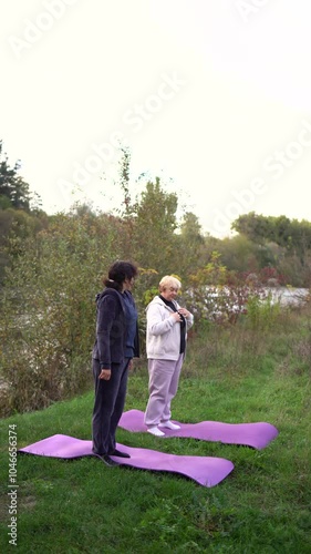 a  middle-aged woman teaches her old mother somatic exercises and yoga to maintain health by the river in autumn photo