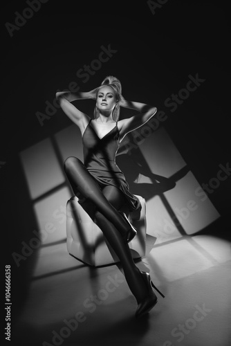 Beautiful blonde woman with perfect legs posing in black tights and high heels - fashion black and white studio photo with window shadows photo