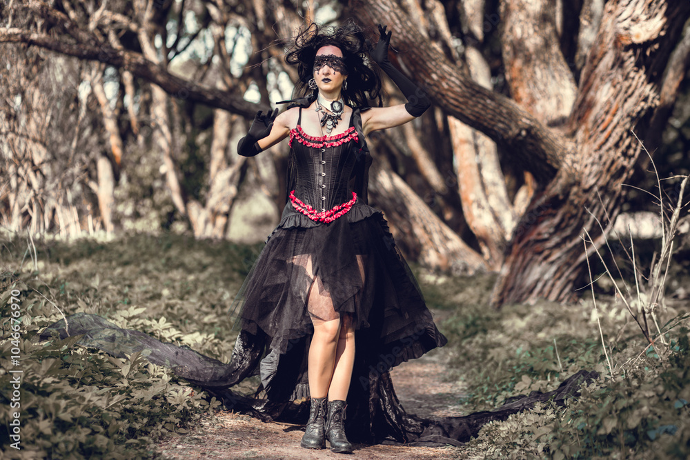 Naklejka premium A young woman in the image of a witch and sorceress, standing in a dark forest, wearing a black dress with a train and a socket on her head.