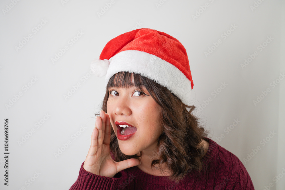Excited young asian woman wearing santa clause hat and red long sleeved sweater is shouting to the audience people, isolated over white background. Concept for Christmas Holiday and New Year Party. Excited young asian woman wearing santa clause hat and red long sleeved sweater is shouting to the audience people, isolated over white background. Concept for Christmas Holiday and New Year Party.
