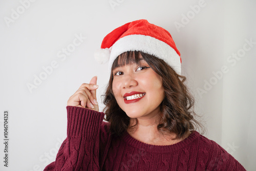 Excited young asian woman wearing santa clause hat and red long sleeved sweater is showing korean love Hand Gestures, isolated over white background. Concept for Christmas Holiday and New Year Party